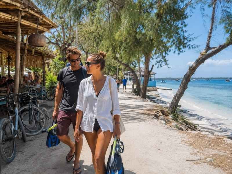 Travelers carrying snorkeling gear along a beachfront path in Gili Trawangan